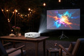 Portable 720p HD home projector on a garden table projecting outdoors at night with string lights
